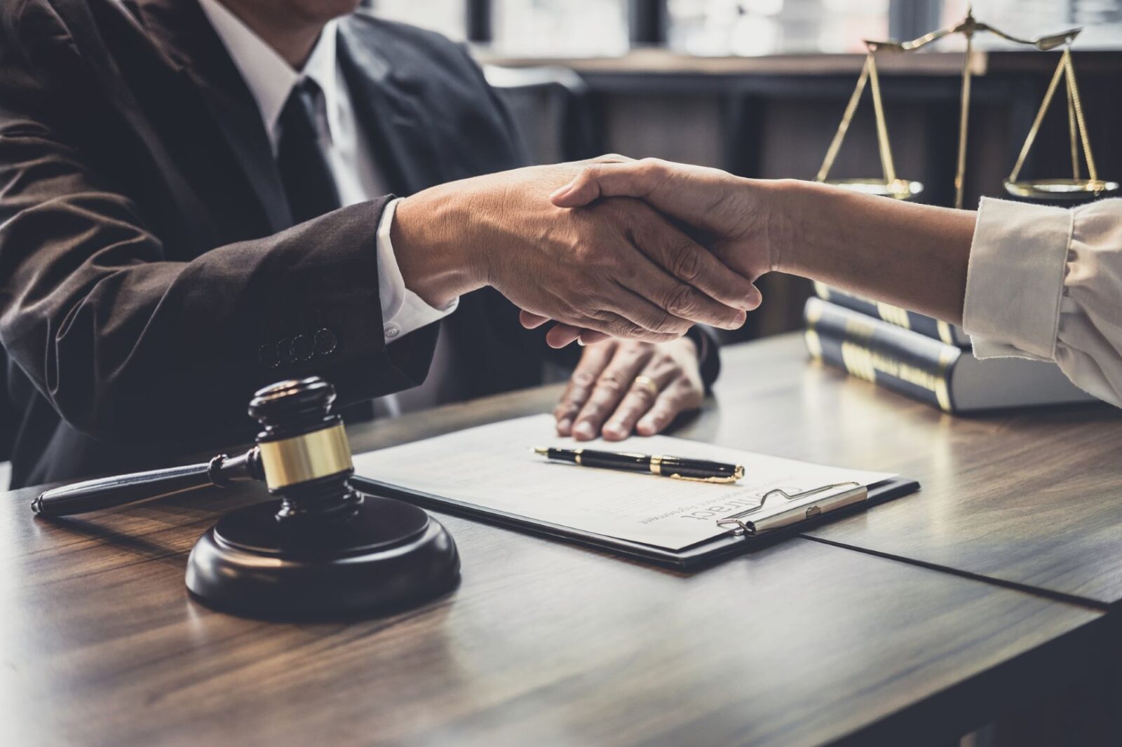 attorney and client meet and shake hands over desk in law firm office
