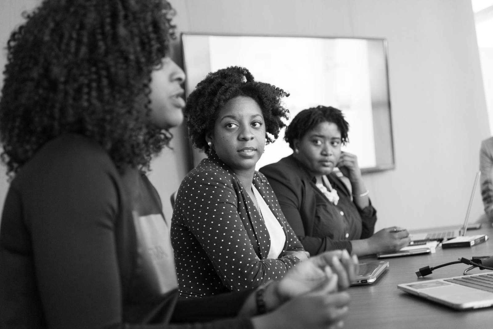 Two women listen as a third speaks about client retention at a table in a conference room.
